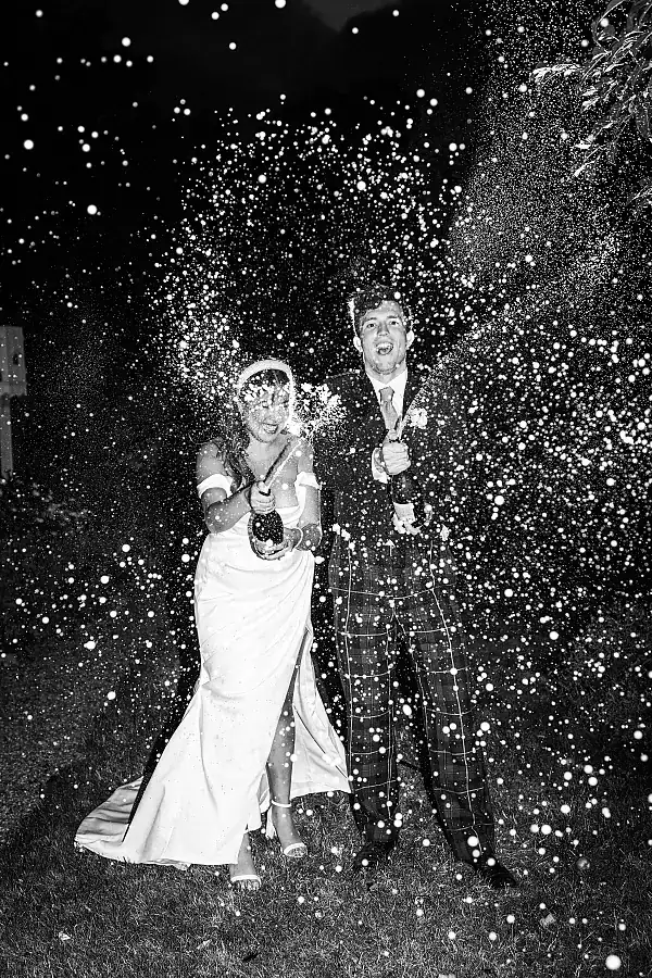 How do we book - black and white shot of bride and groom spraying champagne