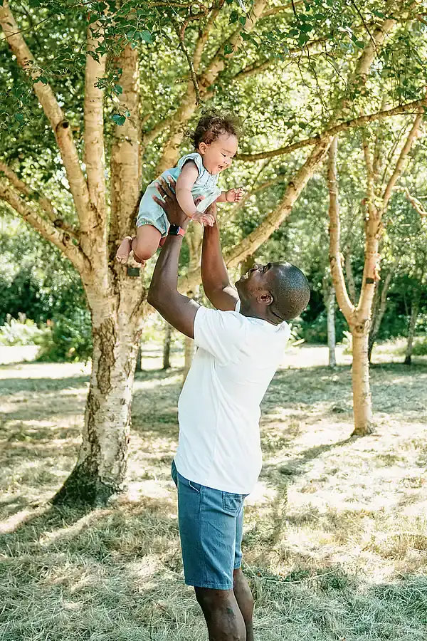 Dad holding child in the air among the trees.